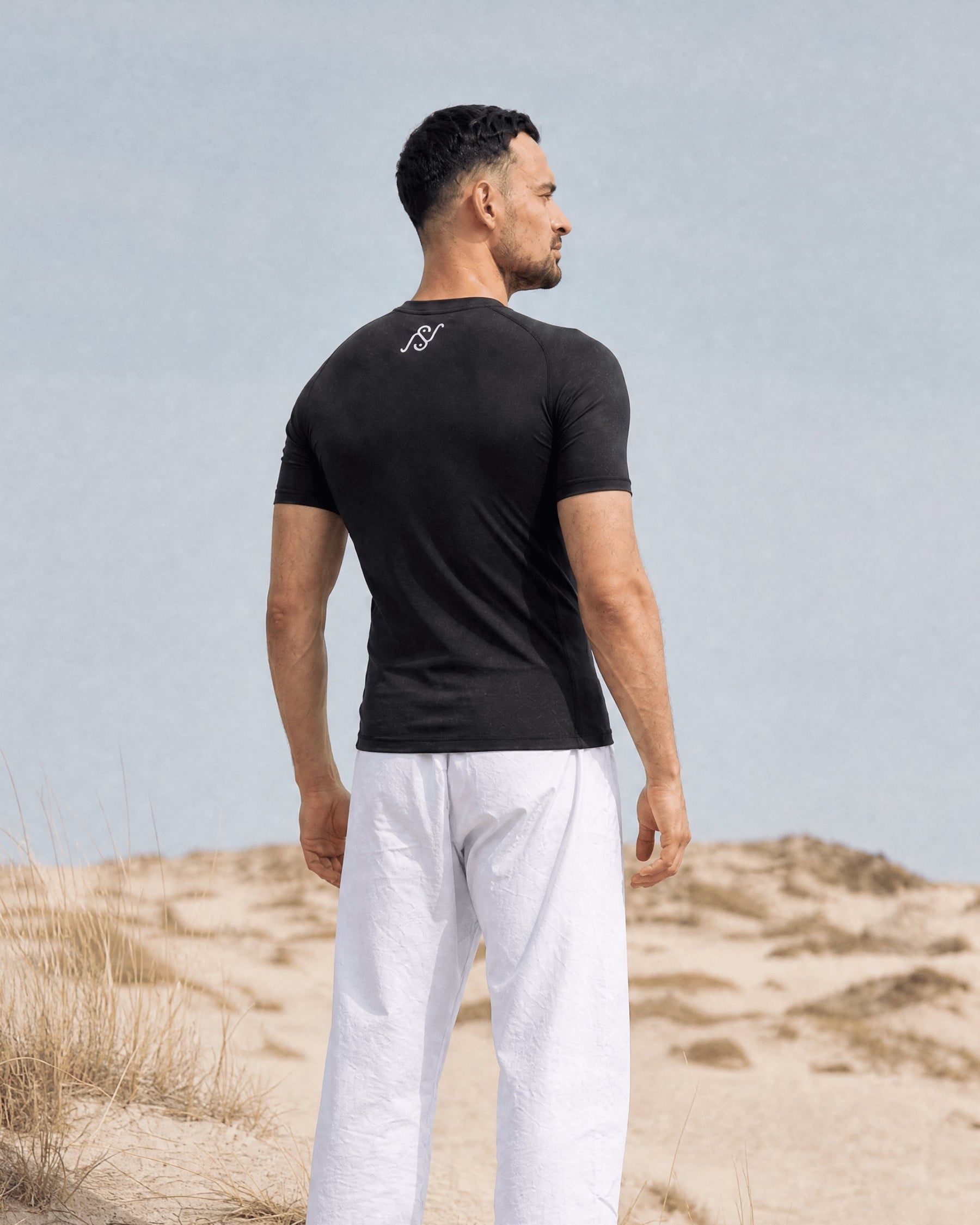 Back view of a man in the black V1 short sleeve rashguard, white NS monogram at the neck