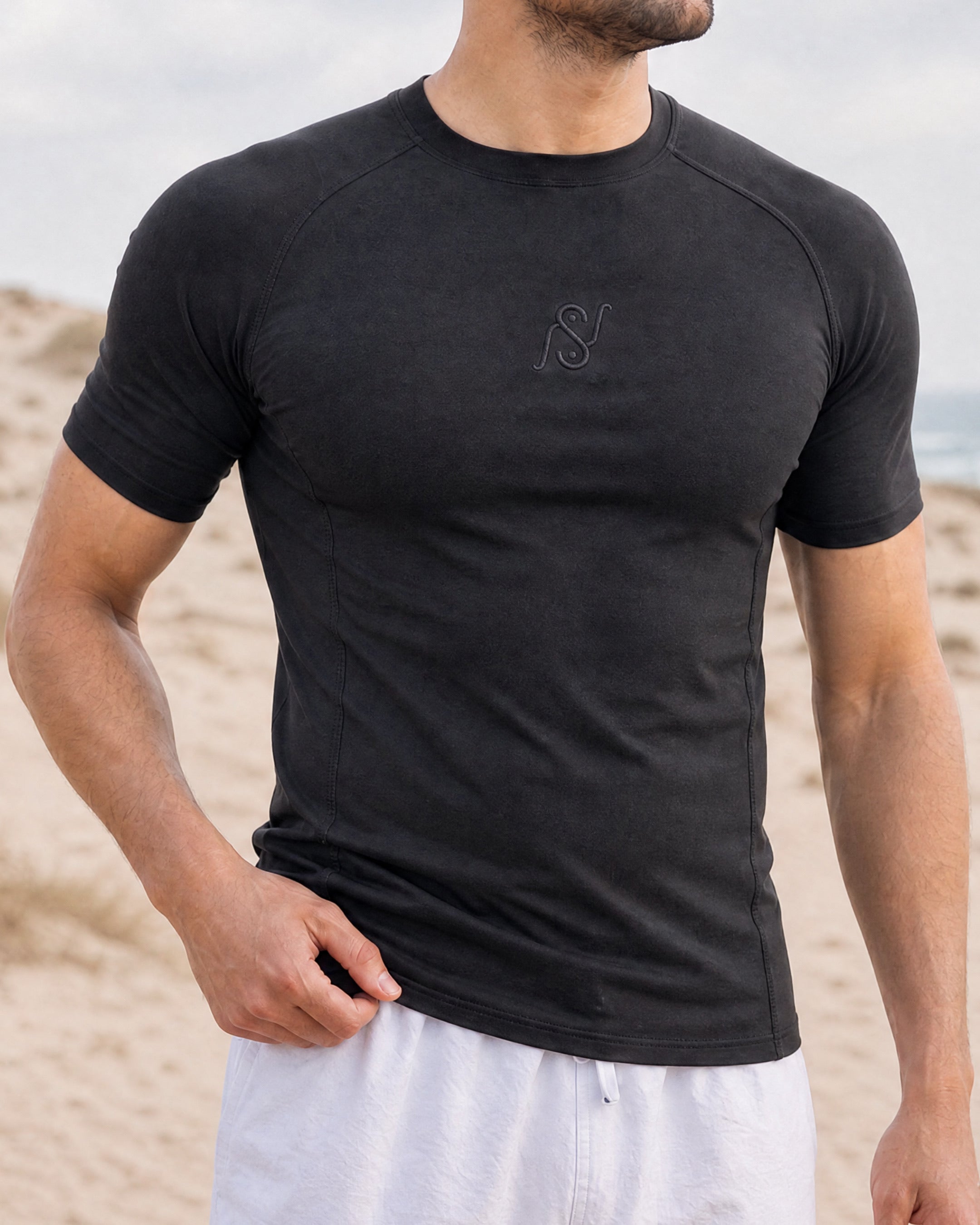 Front close-up of black V1 rashguard, tonal NS monogram embroidered on the chest